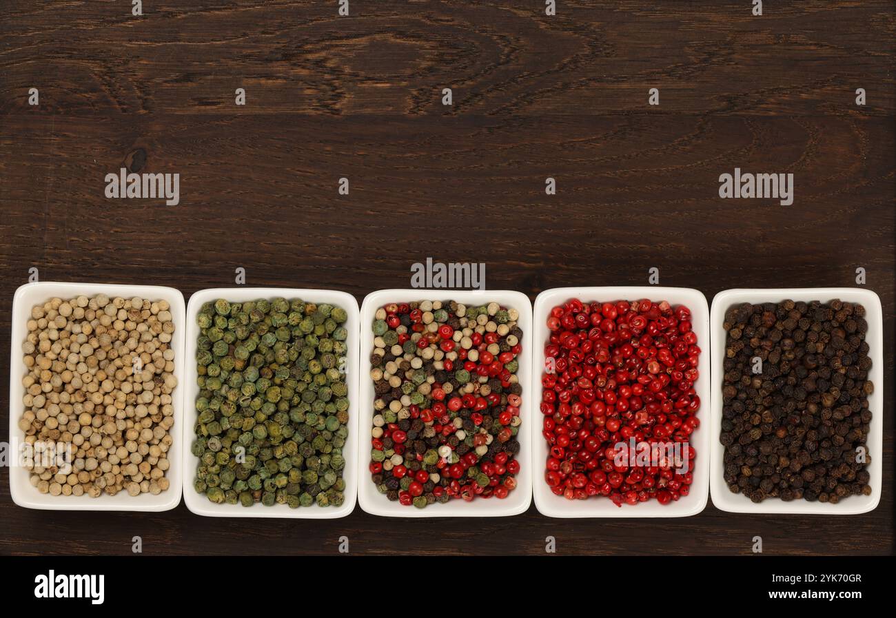 Bols en céramique blanche de grains de poivre assortis, noir, vert, rose, blanc et mélangé sur fond de table en bois foncé avec espace de copie, vue de dessus surélevée, Banque D'Images
