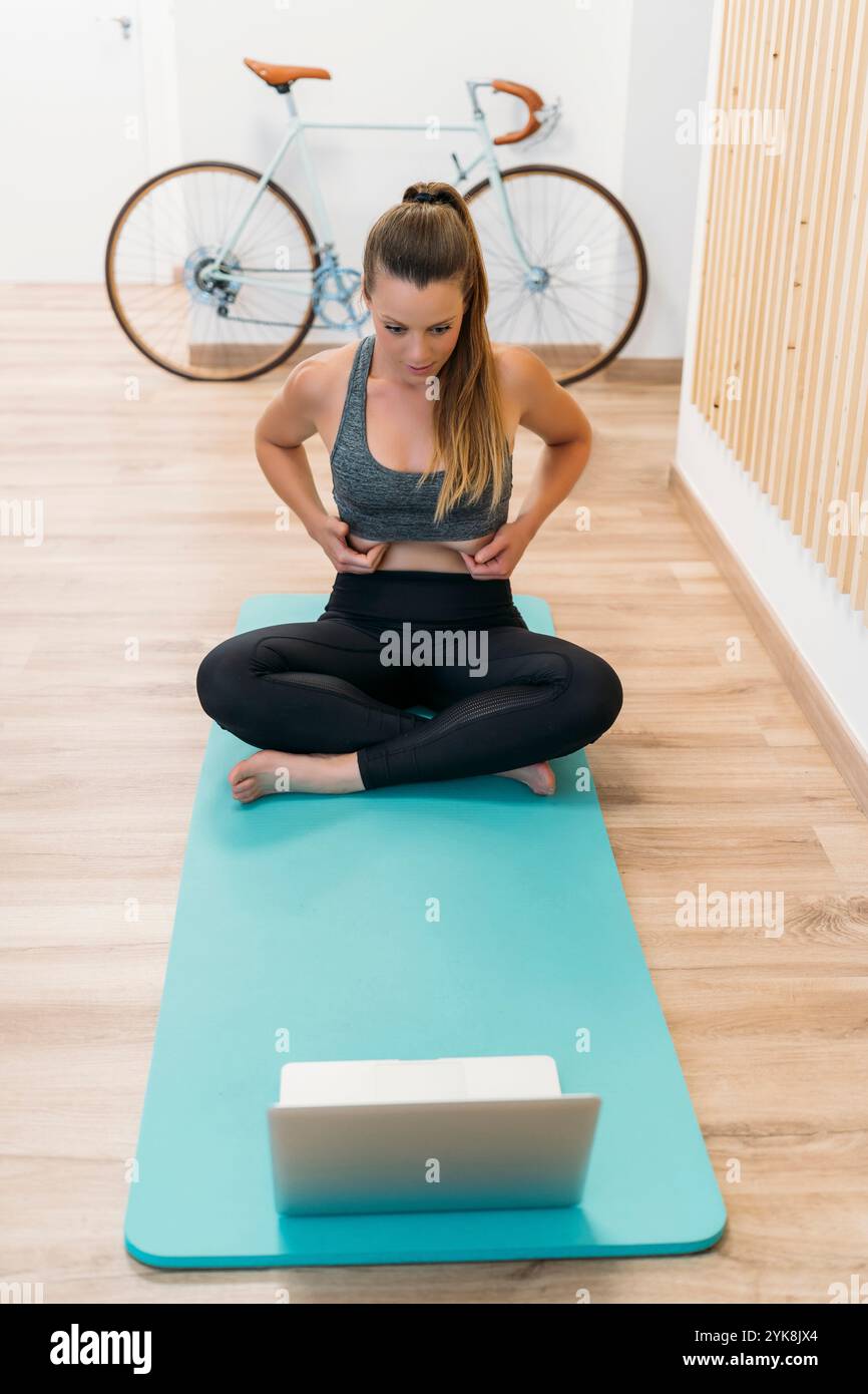 Jeune femme vérifiant sa graisse corporelle regardant des cours de fitness en ligne sur ordinateur portable à la maison Banque D'Images