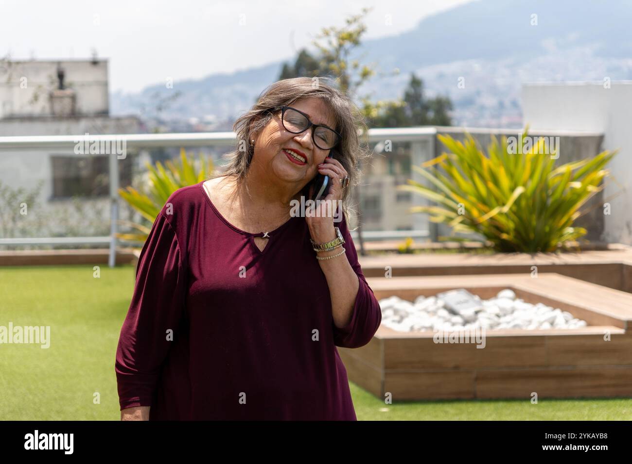 Femme senior en blouse Bourgogne parlant sur le téléphone portable sur la terrasse un matin d'été Banque D'Images