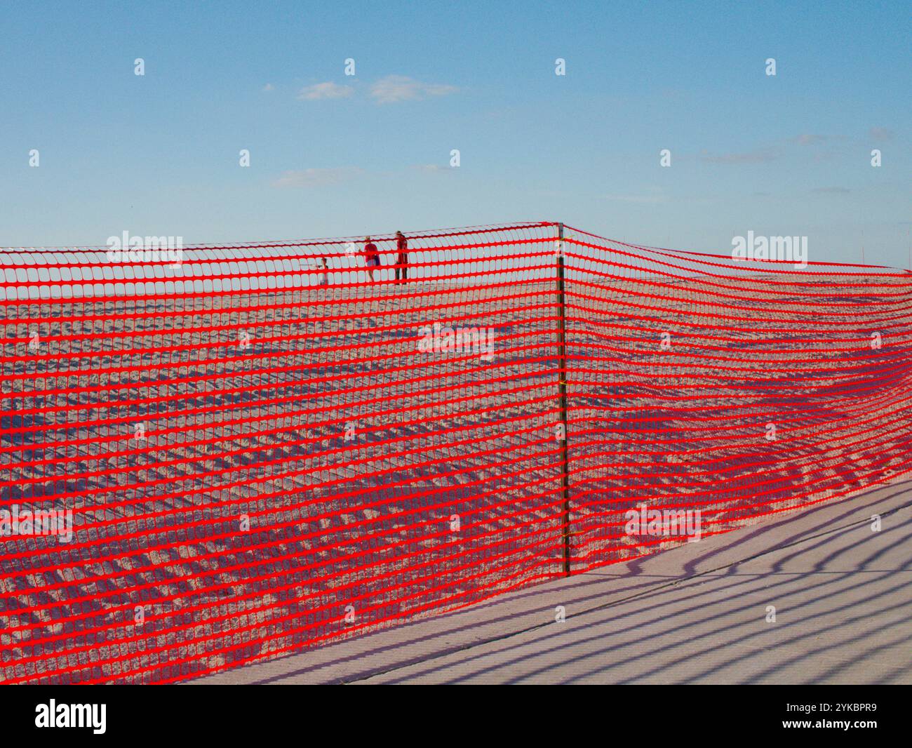 Large vue sur le trottoir à travers la barrière de sécurité orange à 3 personnes sur la plage de sable vers le golfe du Mexique. Traces de pneus dans la restauration de plage de dunes de sable. Banque D'Images