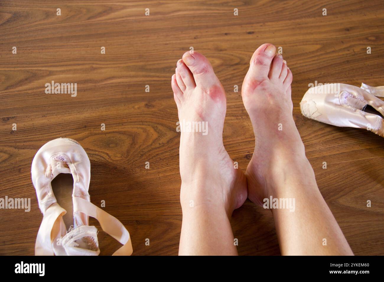 pieds fatigués et rincés de ballerine assis sur un plancher de bois près de ses chaussures pointe utilisées Banque D'Images
