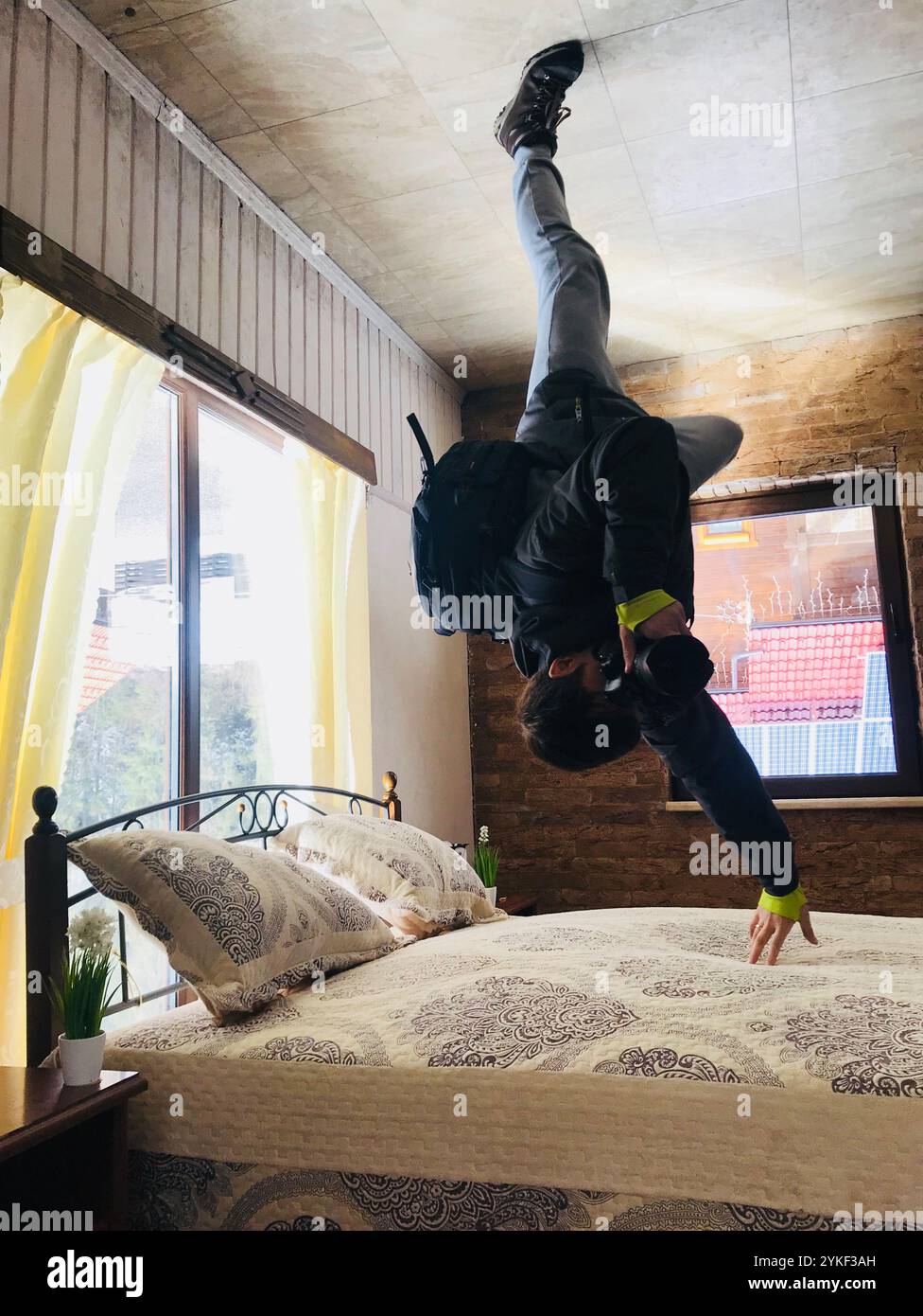 Un homme exécute un mouvement de breakdance dynamique sur le plafond d'une chambre élégante, créant une illusion visuelle intrigante. La chambre est lumineuse et bien déco Banque D'Images
