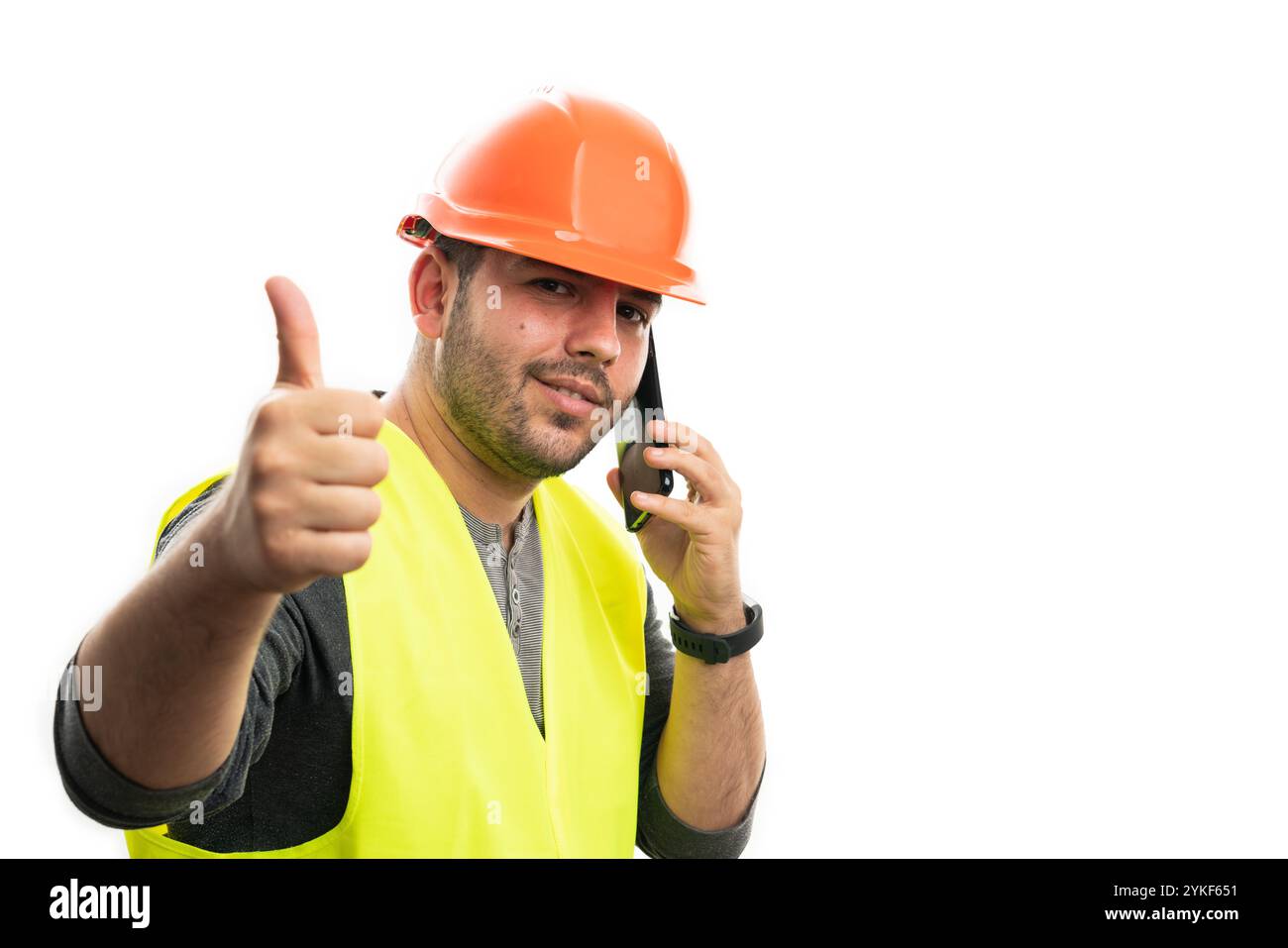 Constructeur masculin souriant portant un casque de sécurité et gilet fluorescent parlant au téléphone faisant le pouce vers le haut comme un geste avec copie vide isolé sur b blanc Banque D'Images
