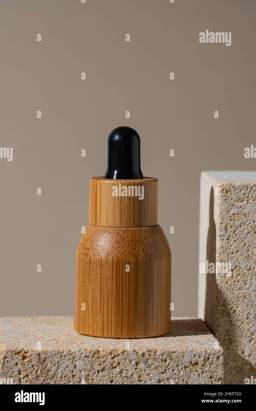 Une composition minimaliste comprend un flacon compte-gouttes en bambou positionné sur un podium en pierre à texture sablonneuse, avec des tons neutres améliorant l'esthétique naturelle Banque D'Images