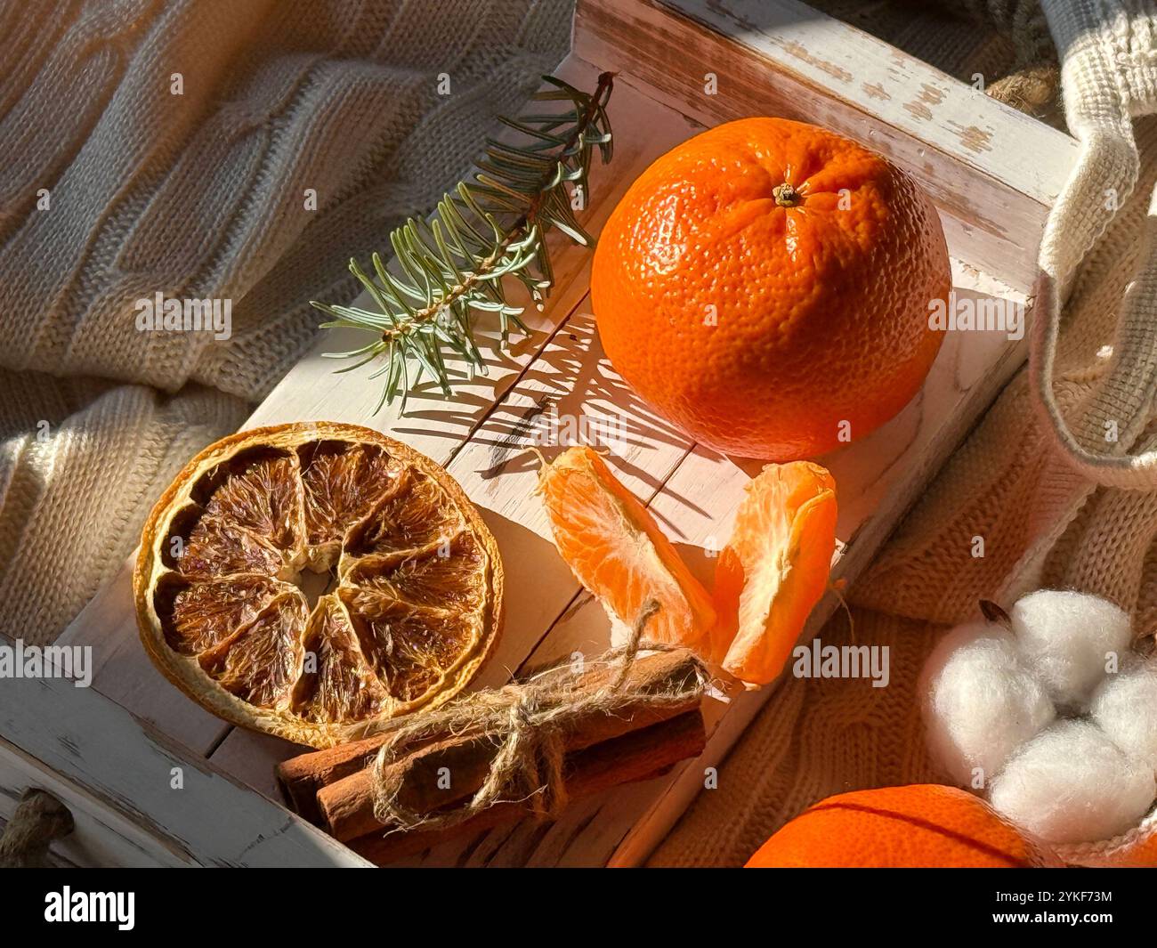 D'en haut, une scène chaleureuse et accueillante avec des mandarines fraîches sur un fond tricoté texturé, accompagnée de tranches d'orange séchées et de bornes de coton doux. Banque D'Images