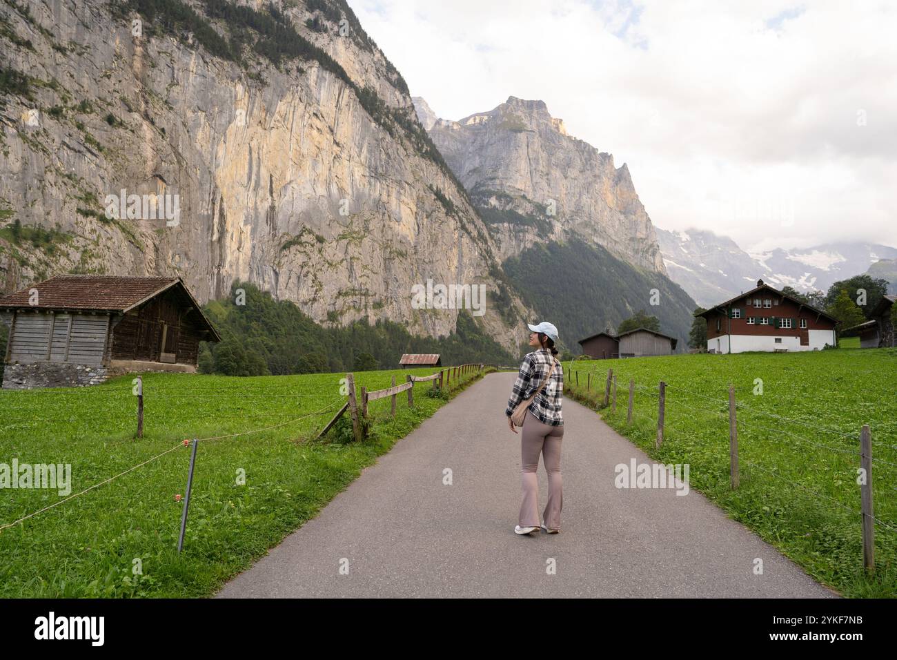 Dans le cadre pittoresque de Lauterbrunnen, en Suisse, une femme se tient sur un chemin rural, contemplant les majestueuses falaises qui l’entourent Banque D'Images