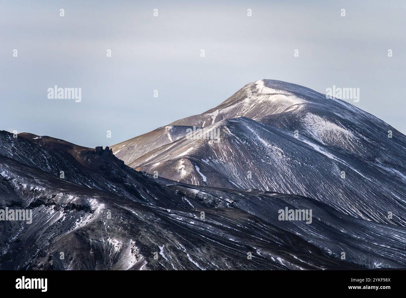 Une vue imprenable sur un sommet de montagne enneigé dans les Highlands islandais, mettant en valeur ses pentes lisses et courbes sous une lumière douce. Banque D'Images