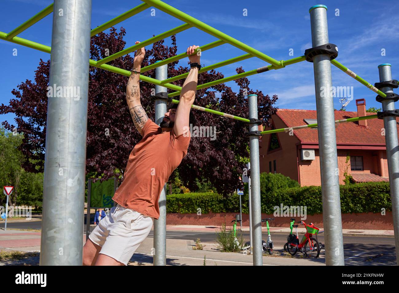 Un jeune athlète effectue des tractions dans un parc de calisthenics en plein air, faisant preuve de force et de dévouement dans un cadre d'entraînement naturel en plein air. Banque D'Images