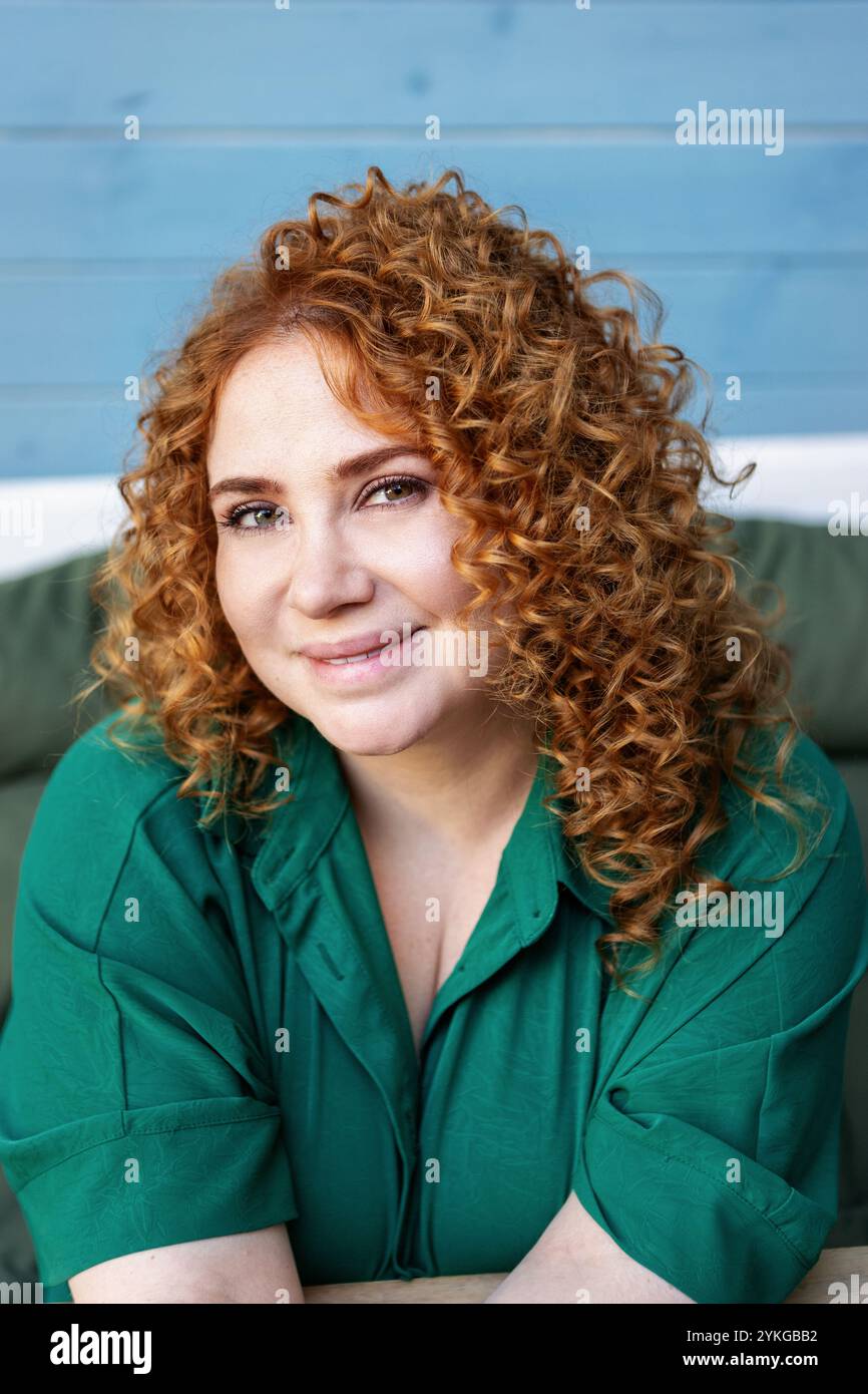 Femme de taille plus avec cheveux rouges bouclés en vêtements verts contre fond de mur en bois bleu coloré, beauté et confiance en extérieur Banque D'Images