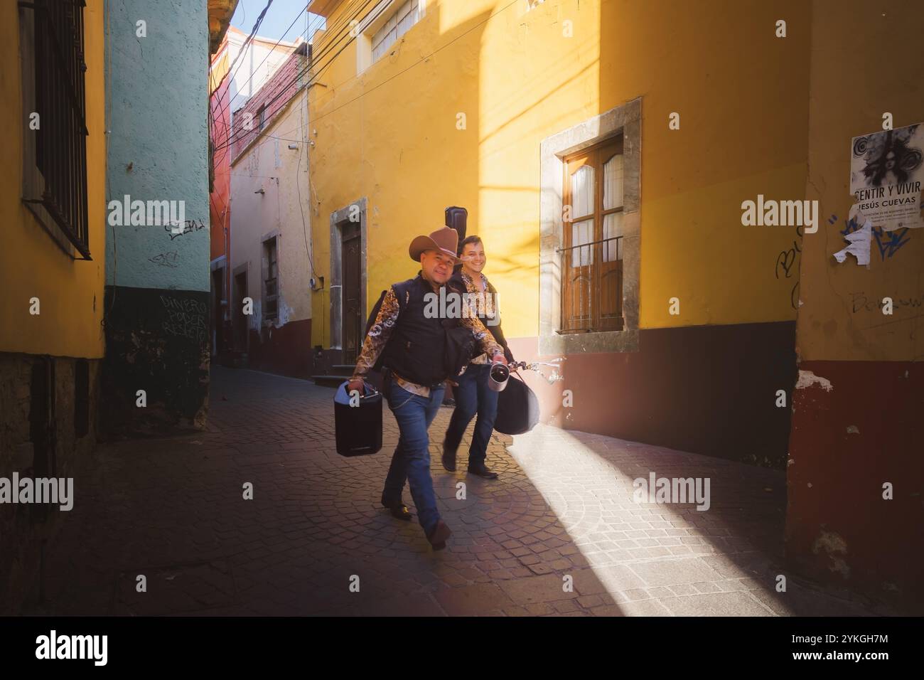 Guanajuato, Mexique - 4 février 2024 : deux musiciens en chapeaux de cow-boy marchent dans une ruelle pavée colorée à Guanajuato, Mexique, portant leur éq Banque D'Images