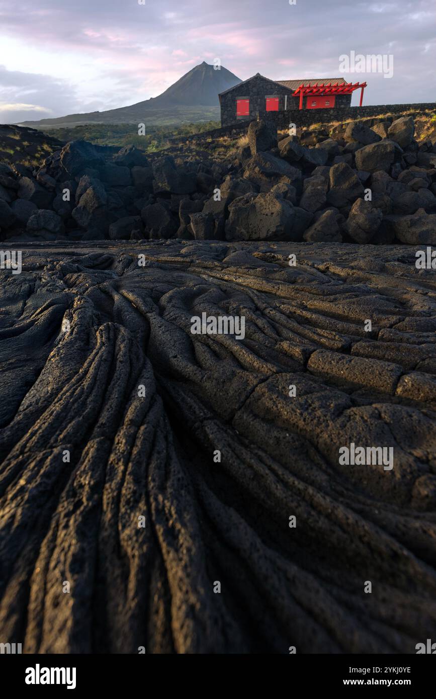 Cabrito, sur l'île de Pico aux Açores, dispose d'une zone de baignade en lave noire avec des maisons traditionnelles en pierre de lave surplombant le majestueux Mont Pico. Banque D'Images
