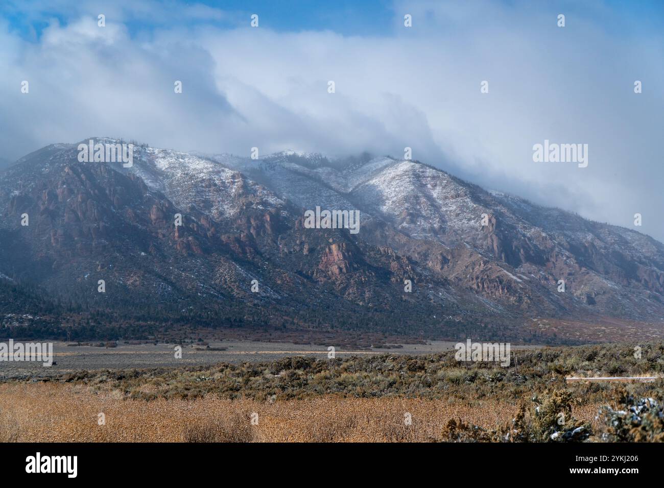 Vue panoramique d'une chaîne de montagnes escarpées avec une légère couche de neige sous un ciel nuageux dramatique surplombant un bassin désertique élevé et sec Banque D'Images