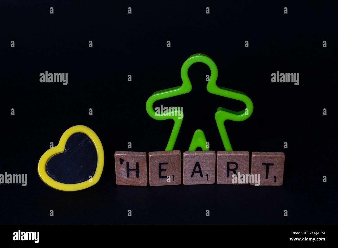 Figurine humaine en plastique pour enfants avec cœur jaune et lettres EN CŒUR, sensibilisation à la Journée mondiale du cœur Banque D'Images