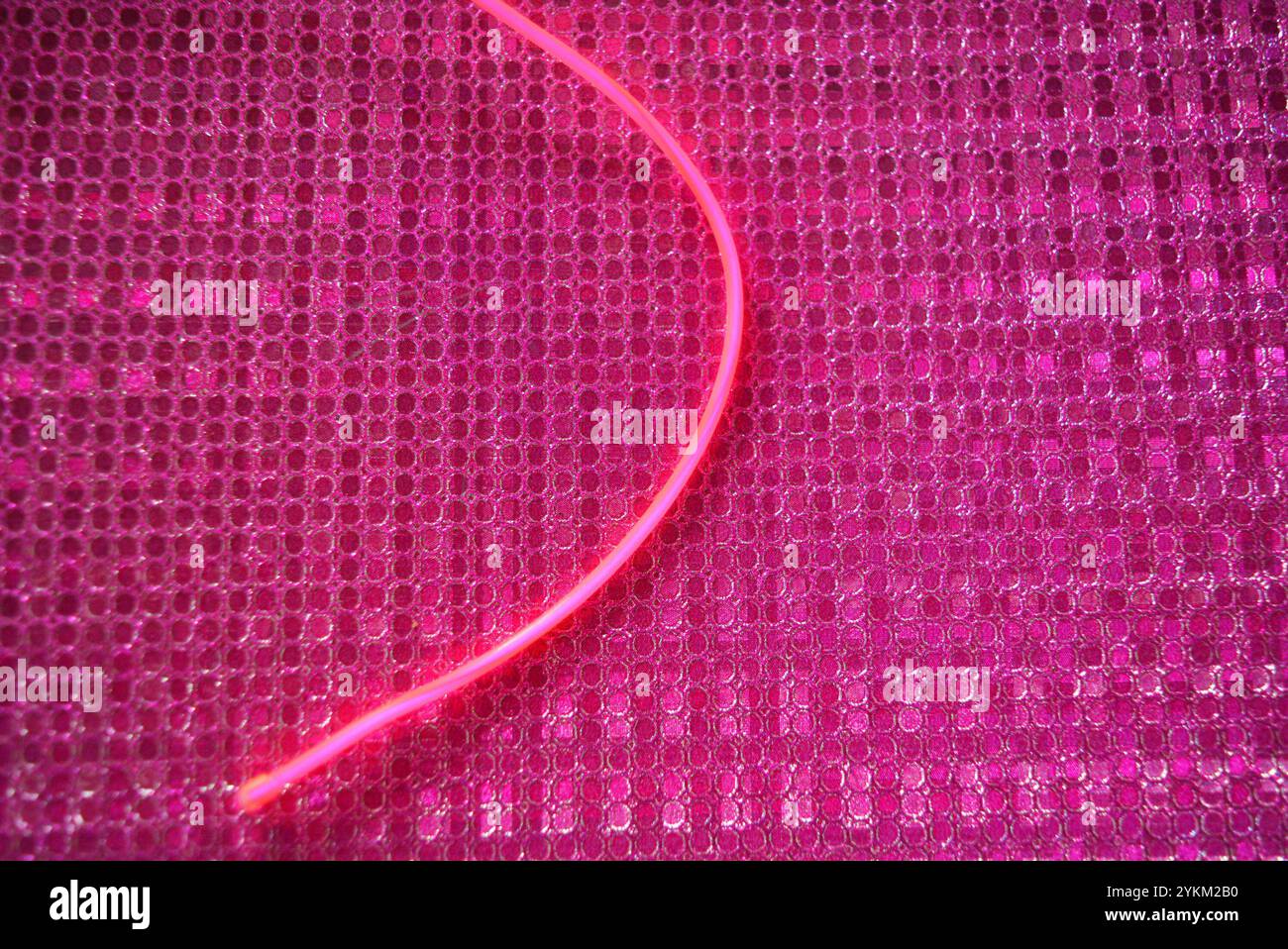 Le fil rose électroluminescent et lumineux inhabituel est situé sur un fond rose vif avec un effet réfléchissant hologramme, de petites particules. Banque D'Images