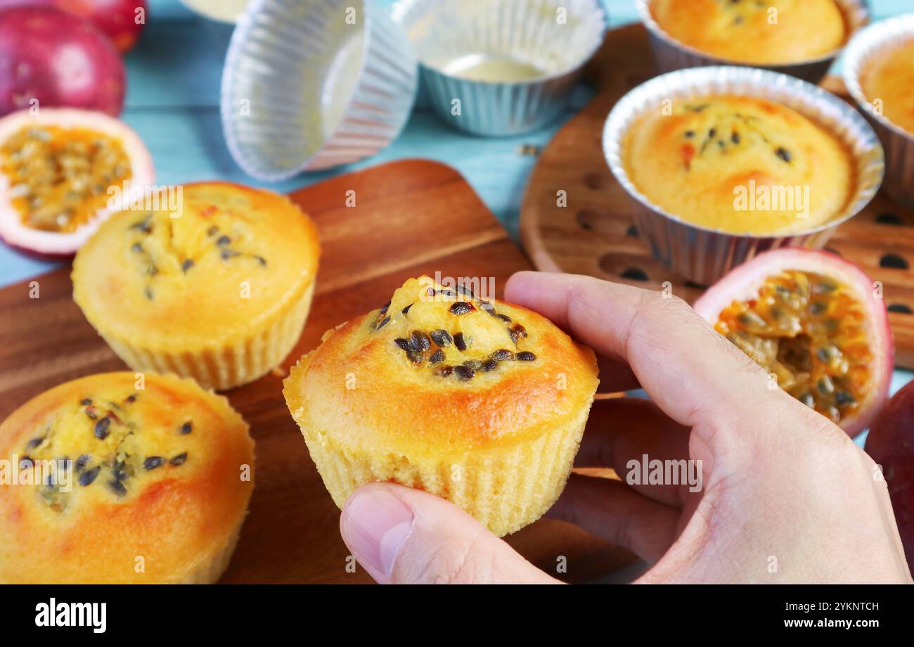 Gros plan de la main tenant un muffin aux fruits de la passion maison fraîchement cuit sur la table de cuisine en désordre Banque D'Images