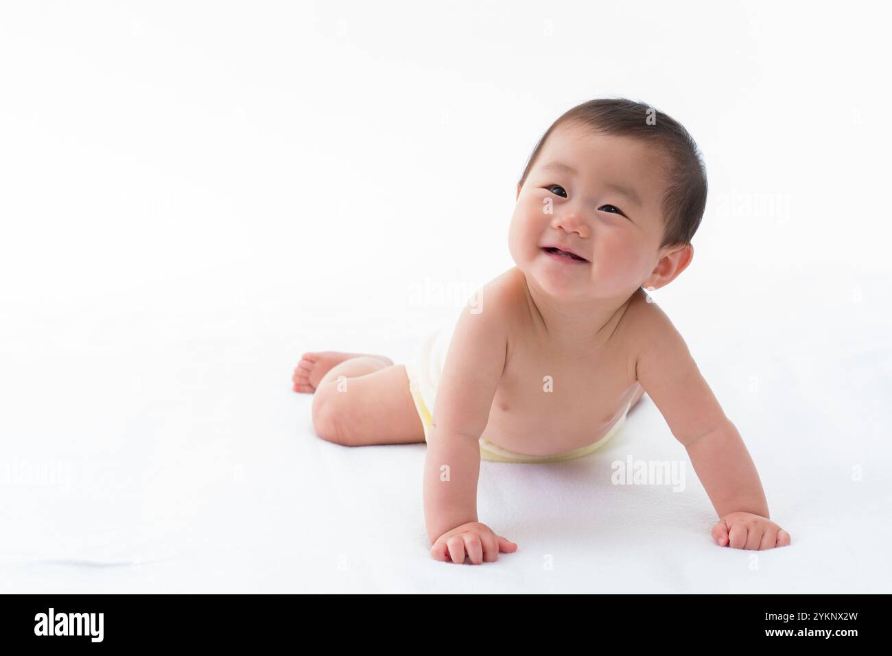 Bébé souriant allongé sur le ventre sur le drap blanc. Banque D'Images