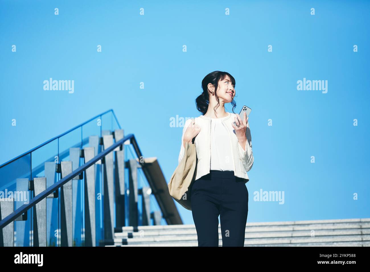 Femme d'affaires marchant à l'extérieur tenant un smartphone Banque D'Images