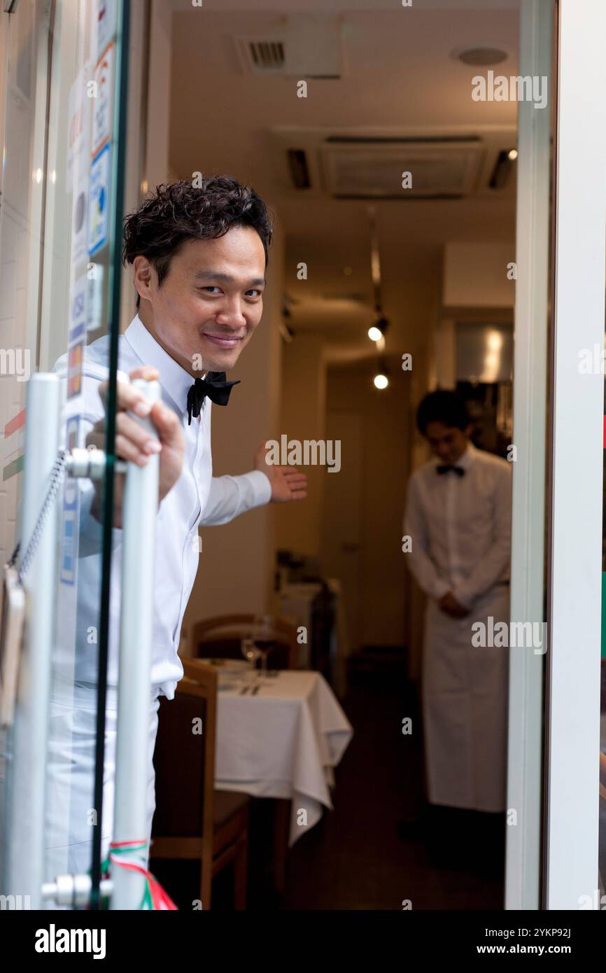Serveur dans le restaurant ouvrant la porte et invitant les clients avec le sourire Banque D'Images