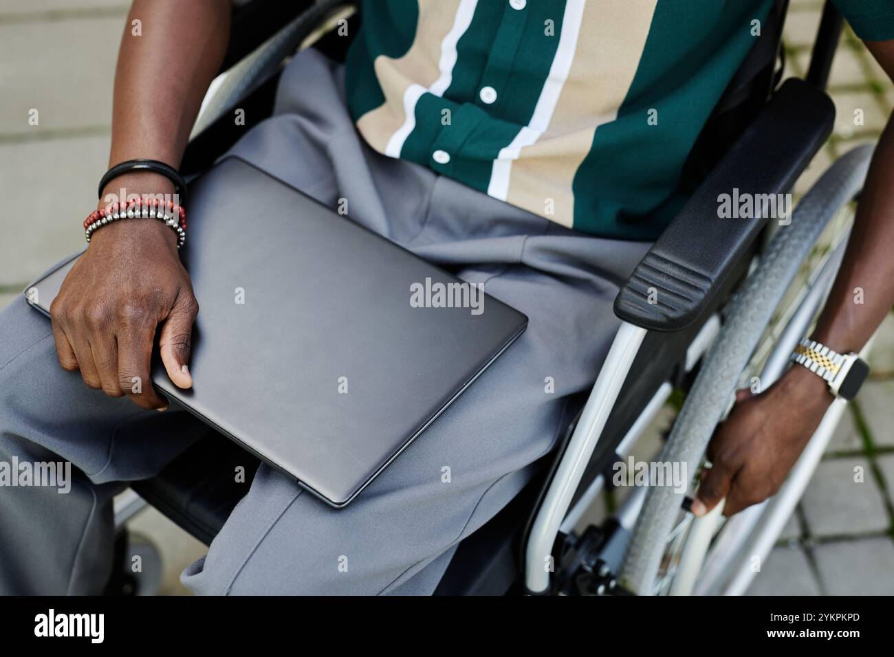 Vue de dessus gros plan de l'homme afro-américain méconnaissable avec un handicap tenant un ordinateur portable et assis dans l'espace de copie en fauteuil roulant Banque D'Images