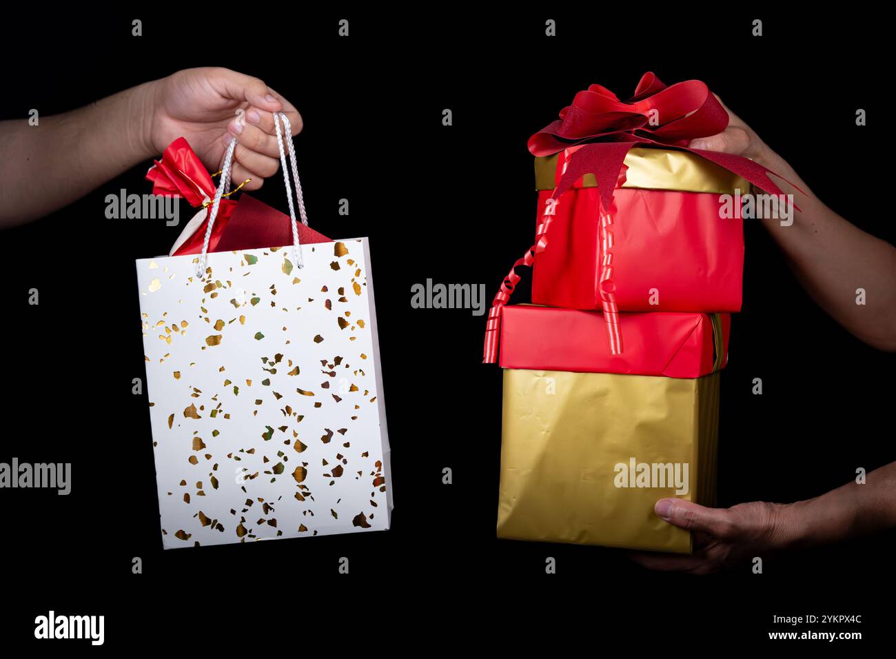 Deux mains échangent des boîtes cadeaux vibrantes et un sac décoratif, symbolisant la célébration et le don. La scène transmet chaleur et joie contre un simple blac Banque D'Images