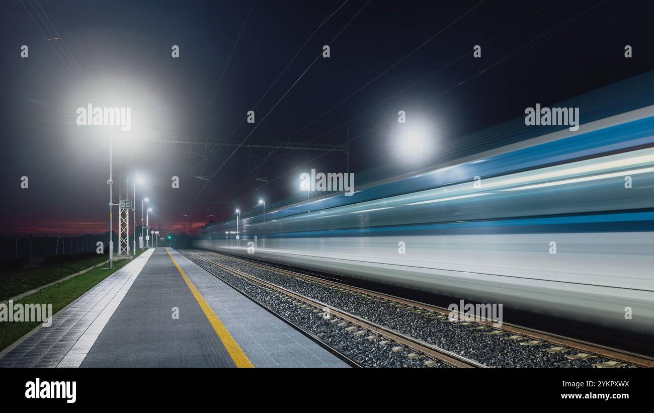 Chemin de fer moderne la nuit. Piste légère de train à grande vitesse dans la gare. Train de voyageurs interurbain en mouvement. Banque D'Images
