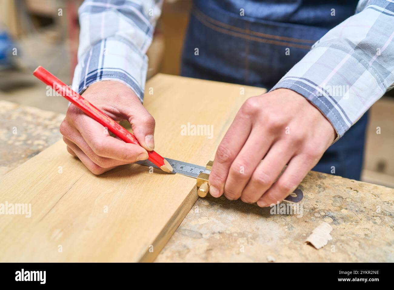 Un menuisier démontre la précision en marquant une planche de bois avec un crayon dans une cour de bois. Cette image met en évidence les compétences et le souci du détail R Banque D'Images