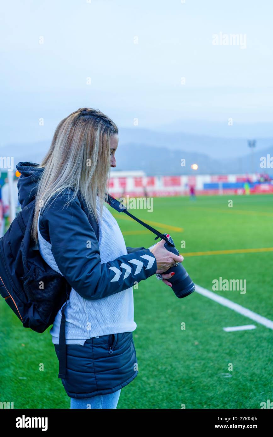 Photographe sportive féminine d'âge moyen examinant des photos sur l'appareil photo lors d'un match de football pendant le crépuscule Banque D'Images