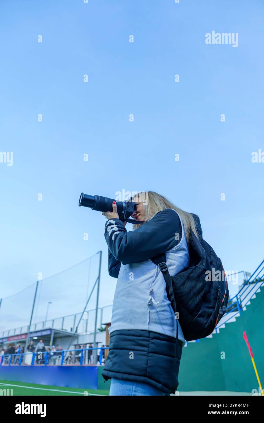 Vue latérale d'une photographe sportive d'âge moyen prenant des photos sur un terrain de football pendant un match au crépuscule Banque D'Images