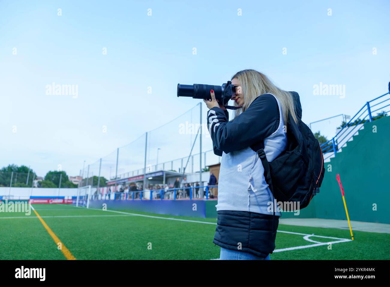 Vue latérale d'une photographe sportive d'âge moyen prenant des photos sur un terrain de football pendant un match au crépuscule Banque D'Images