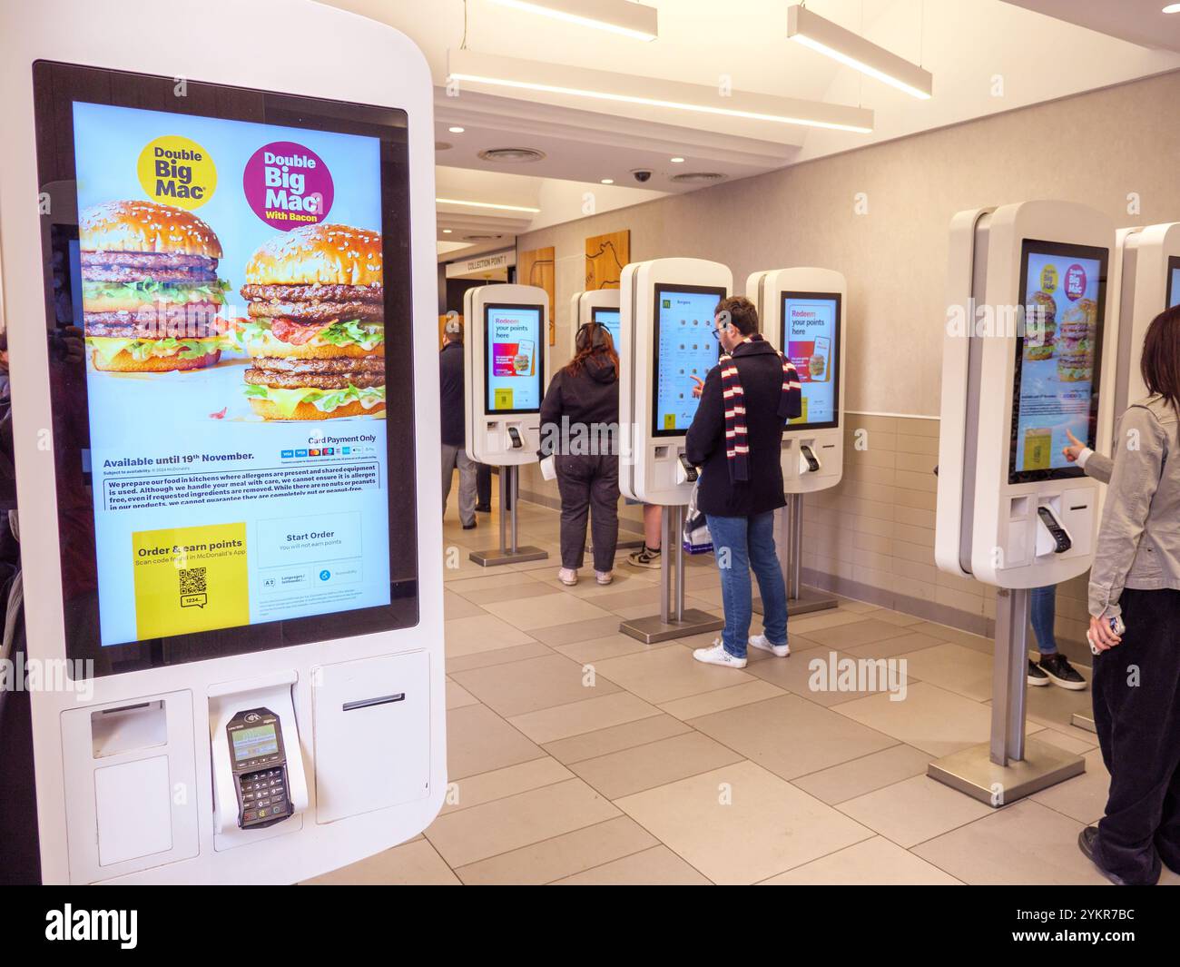 Les gens qui commandent leur fast-food à l'aide de terminaux de commande à écran tactile dans un restaurant McDonald's, au Royaume-Uni Banque D'Images