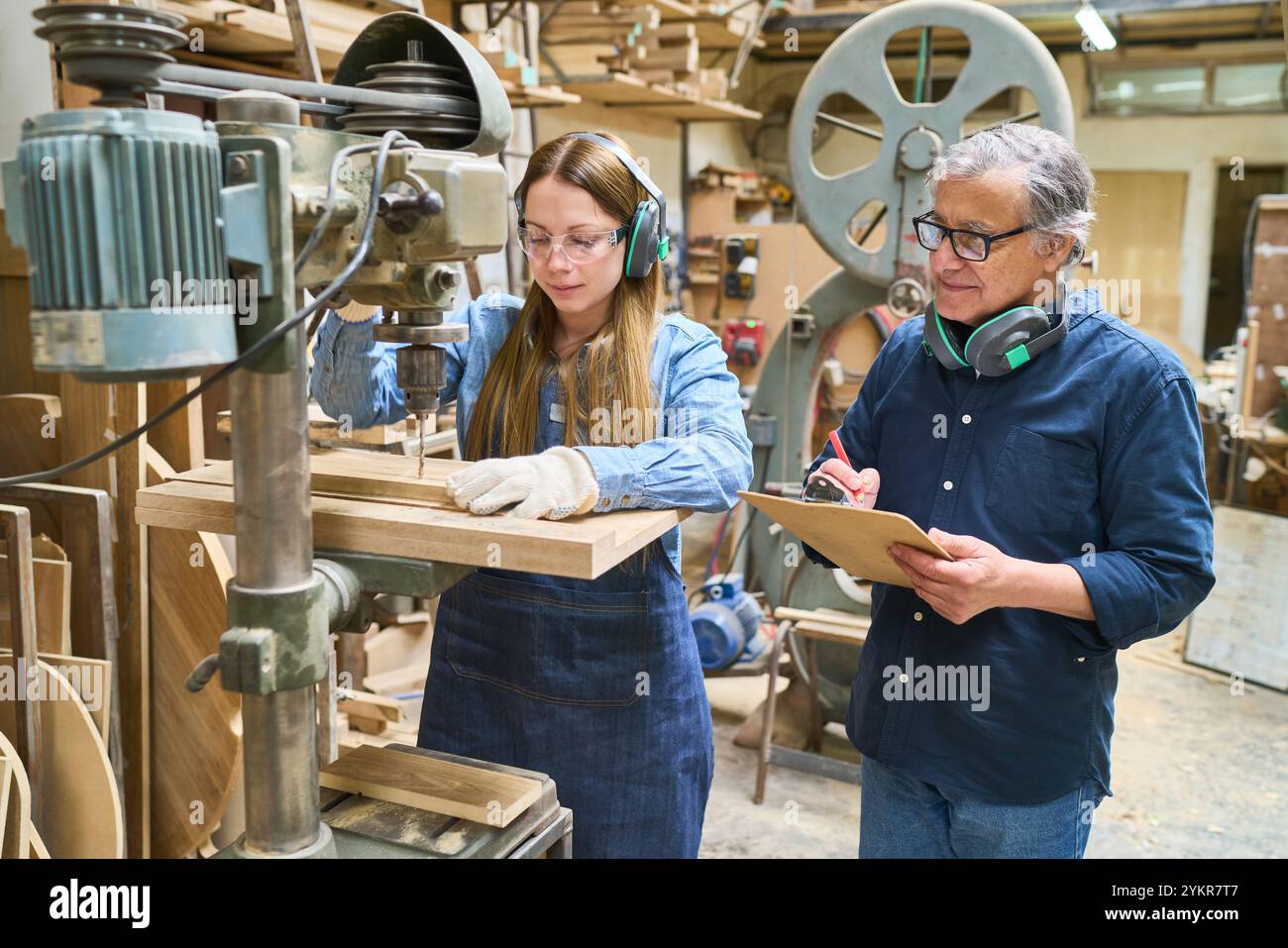 Un jeune apprenti reçoit les conseils d'un mentor expérimenté lorsqu'il travaille sur une machine dans un chantier forestier. La scène met en évidence le travail d'équipe, la formation, un Banque D'Images