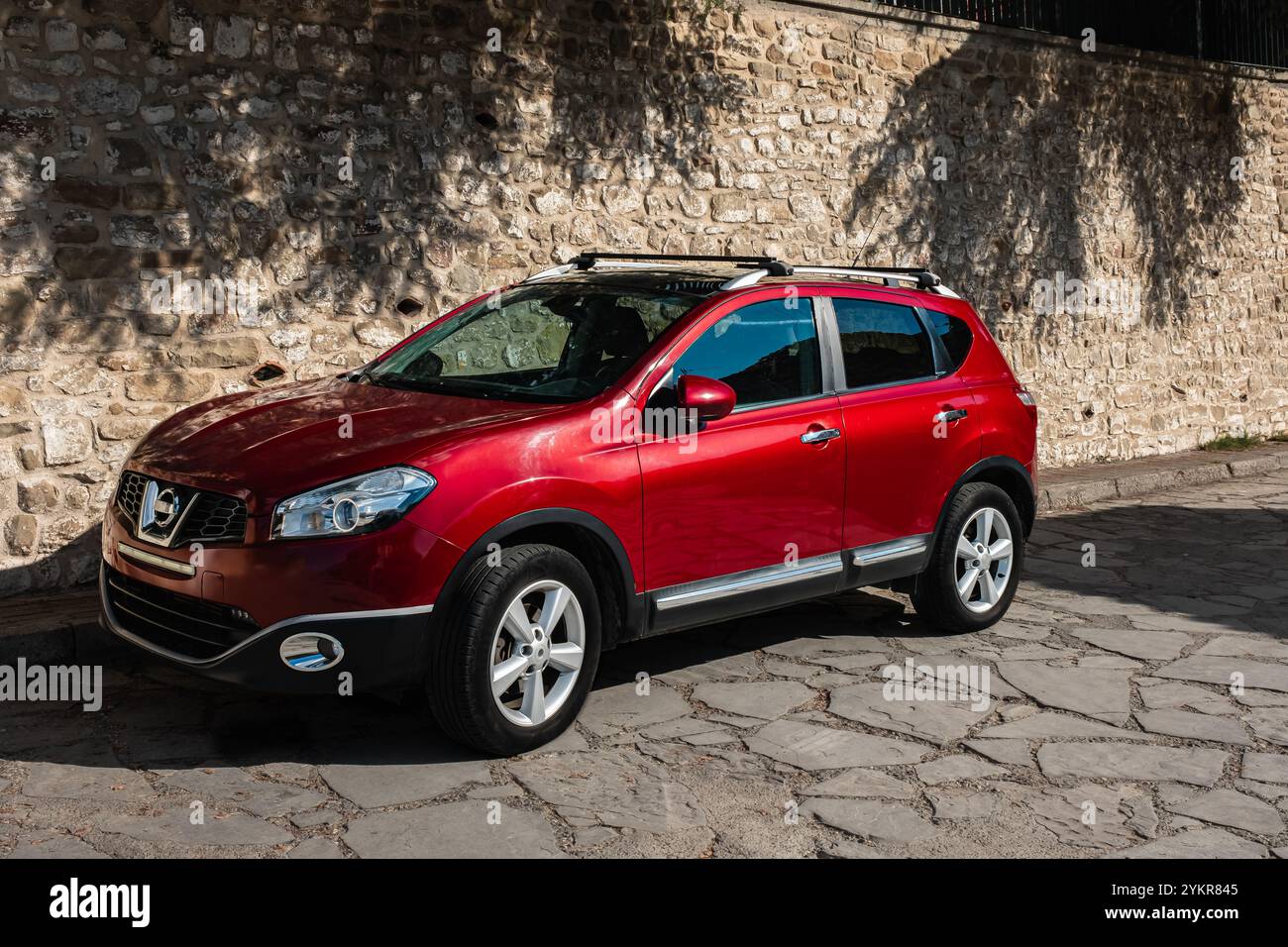Voiture élégante Nouvelle voiture 4 portes. Voiture rouge familiale moderne. Voiture rouge garée sur la rue vide dans une journée ensoleillée. Type de modèle de SUV multisegment sous-compact, vue latérale Banque D'Images