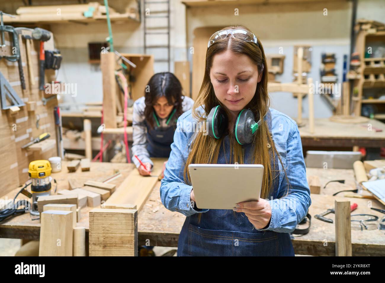 Une jeune femme dans un atelier, apprenant la menuiserie avec les conseils d'un mentor expérimenté. Mettre l'accent sur le travail d'équipe, la formation et le développement des compétences dans un p Banque D'Images