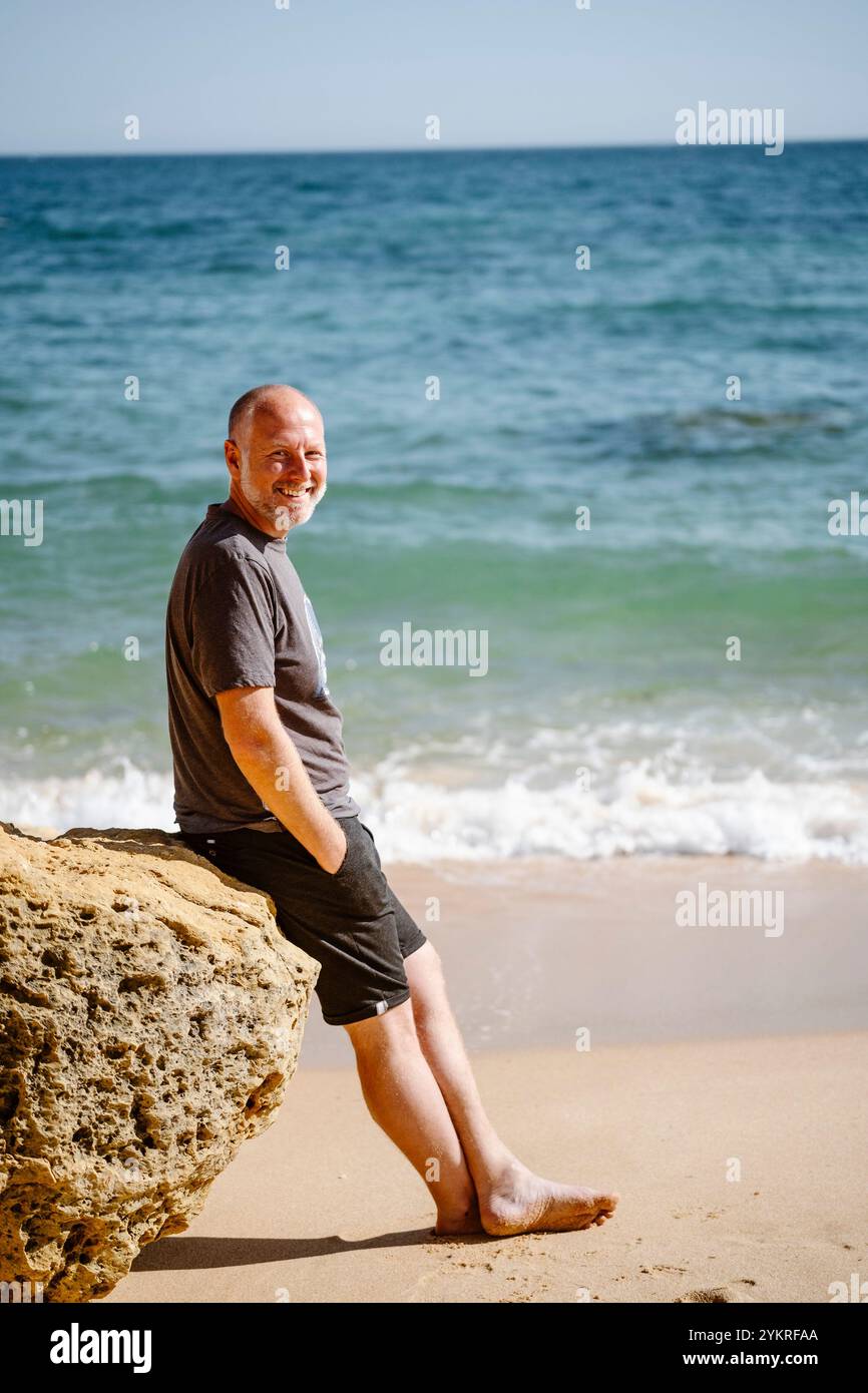 Homme caucasien assis sur un rocher à la plage de São Rafael à Albufeira, Algarve - Portugal Banque D'Images