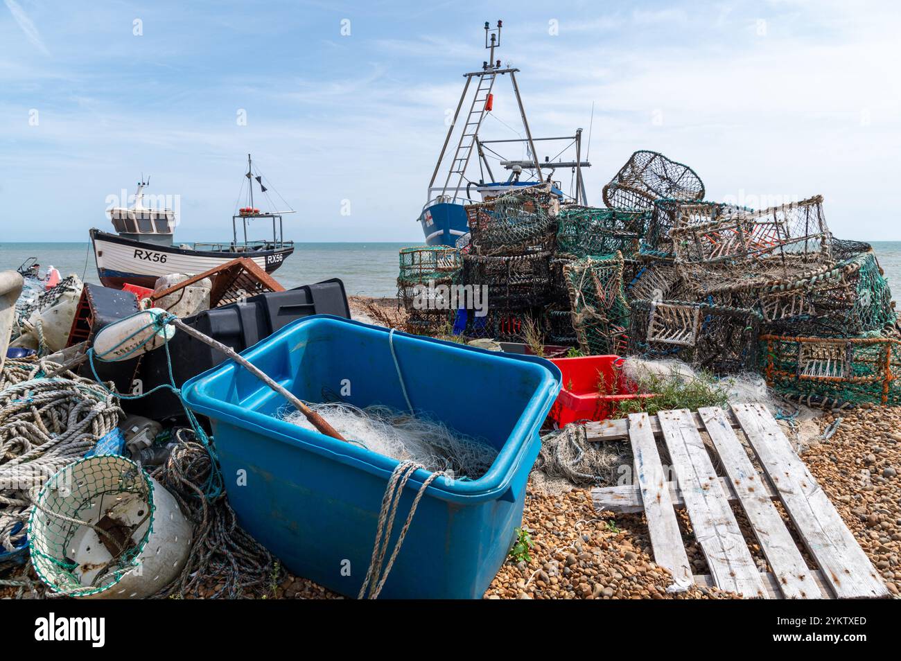 Équipement de pêche sur la plage de Hastings comprenant un filet dans une boîte bleue, des casiers de homard et de crabe, des cordes et deux bateaux de pêche Banque D'Images