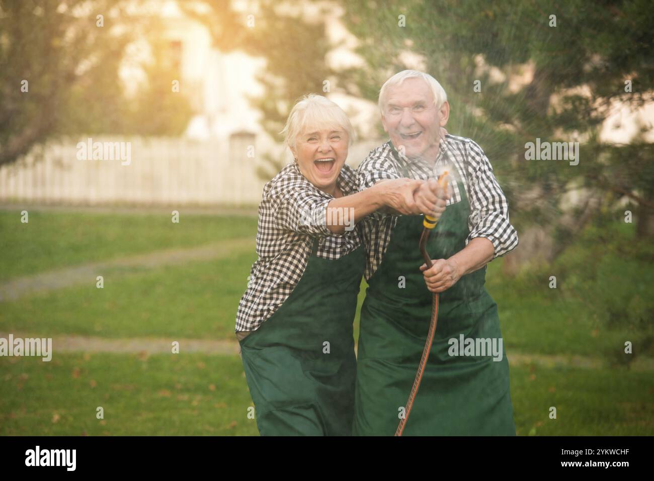 Couple senior s'amusant. Jardiniers et tuyau d'eau Banque D'Images