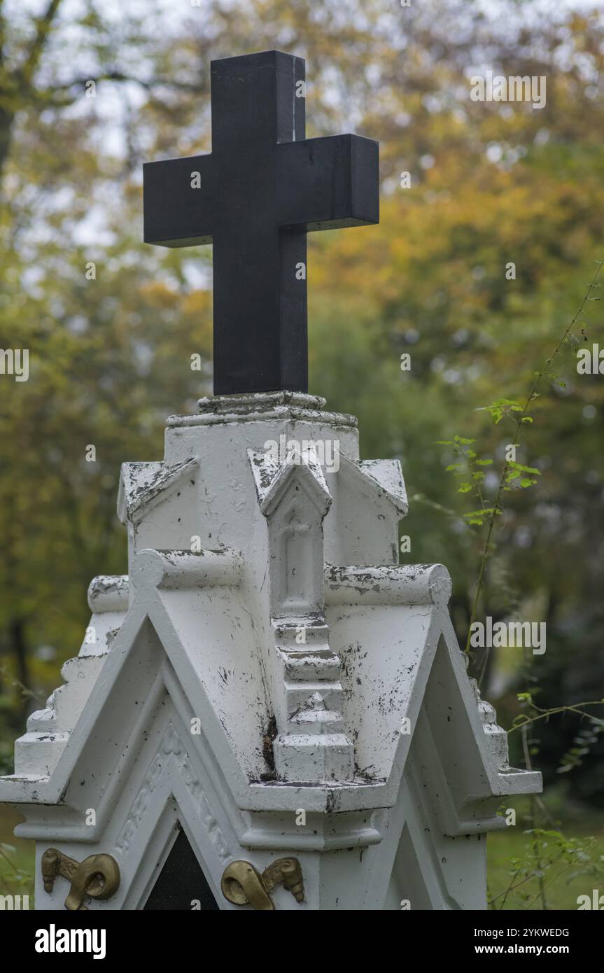 Croix noire s'élevant au-dessus du piédestal blanc altéré dans le cimetière, évoquant les thèmes du souvenir, de la foi et de la mortalité Banque D'Images