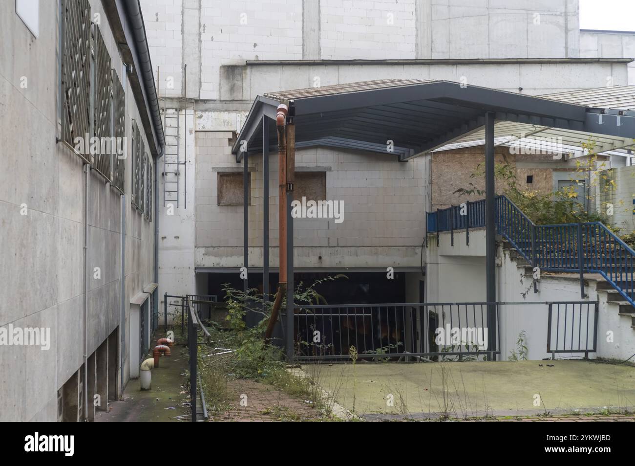 Bâtiment industriel désolant avec des fenêtres en bois, des mauvaises herbes envahies et des infrastructures en décomposition, symbolisant la décomposition urbaine et le déclin économique Banque D'Images