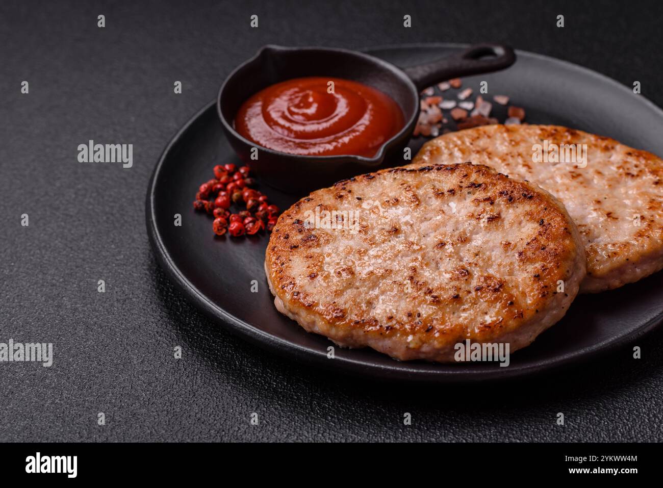 Côtelette de hamburger de poulet grillé avec sel, épices et herbes sur un fond de béton foncé Banque D'Images