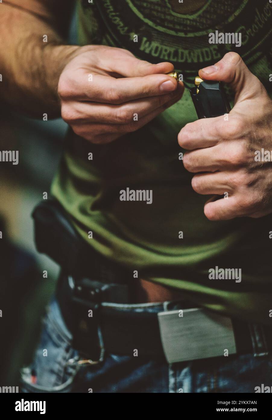 Homme chargeant des balles dans un magasin, qui appartient probablement à une arme à feu. porter des vêtements décontractés, y compris une chemise verte et un jean. Il y a aussi un Banque D'Images