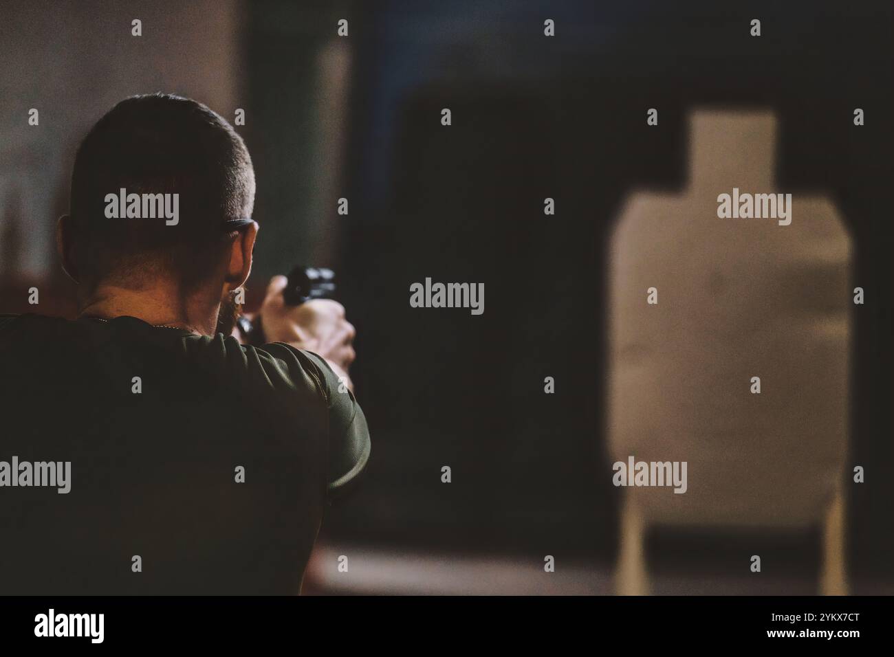 Homme pointant une arme à feu vers une cible sur ce qui semble être un champ de tir intérieur. l'homme est vu de derrière, se concentrant sur la cible en face d'eux. Banque D'Images