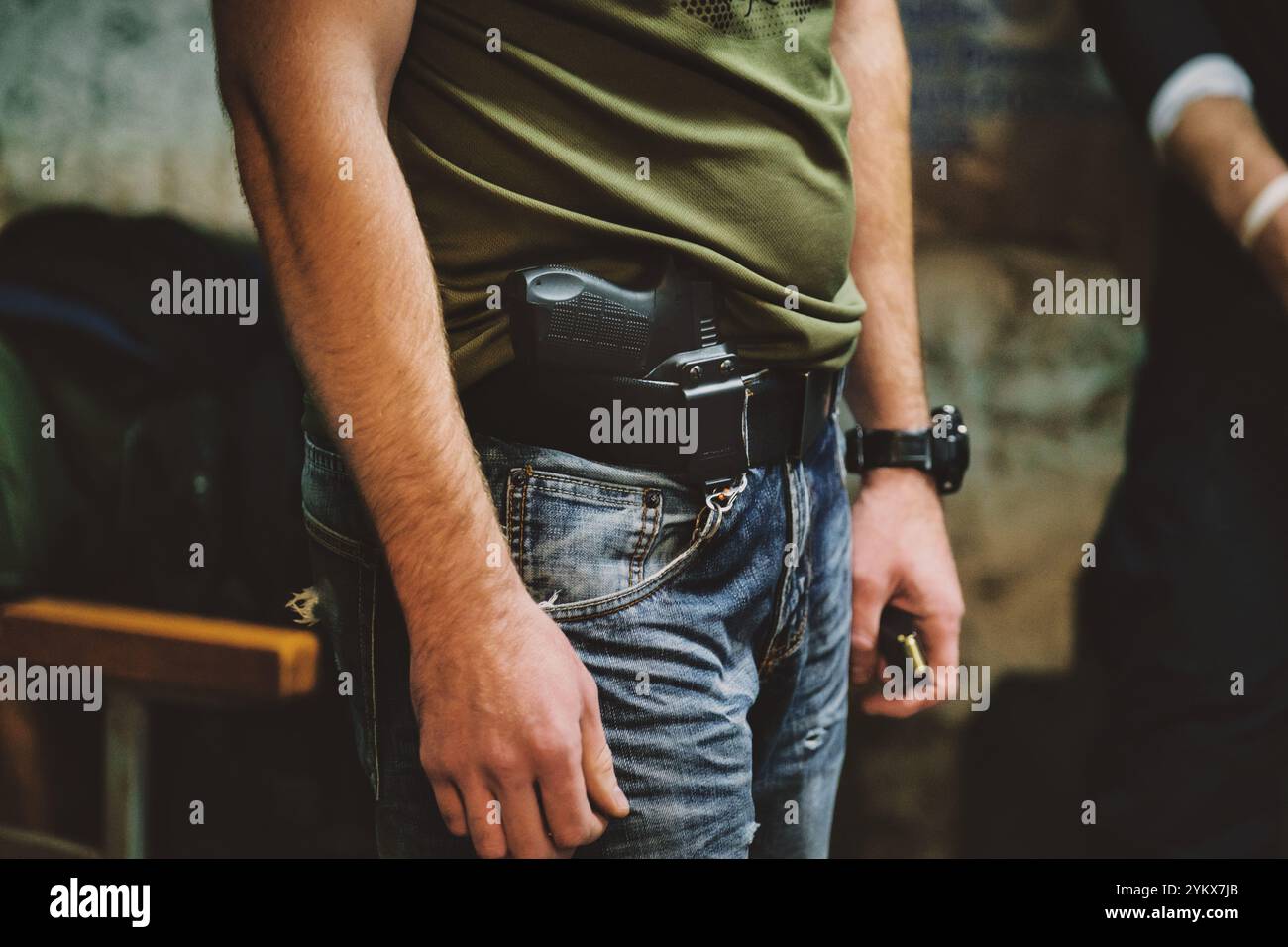 Homme portant un Jean et une chemise verte. La personne a une arme de poing tenue à la taille. Banque D'Images