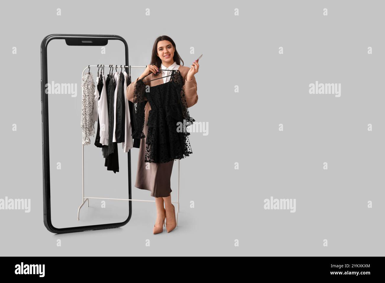 Grand téléphone portable et jeune femme avec des vêtements élégants sur cintre sur fond gris Banque D'Images
