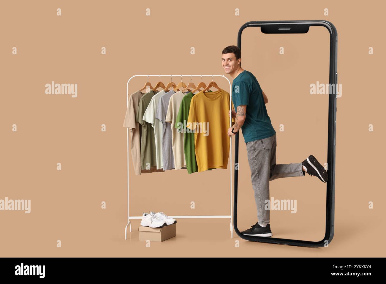 Grand téléphone portable et jeune homme avec des vêtements élégants sur cintre sur fond beige Banque D'Images
