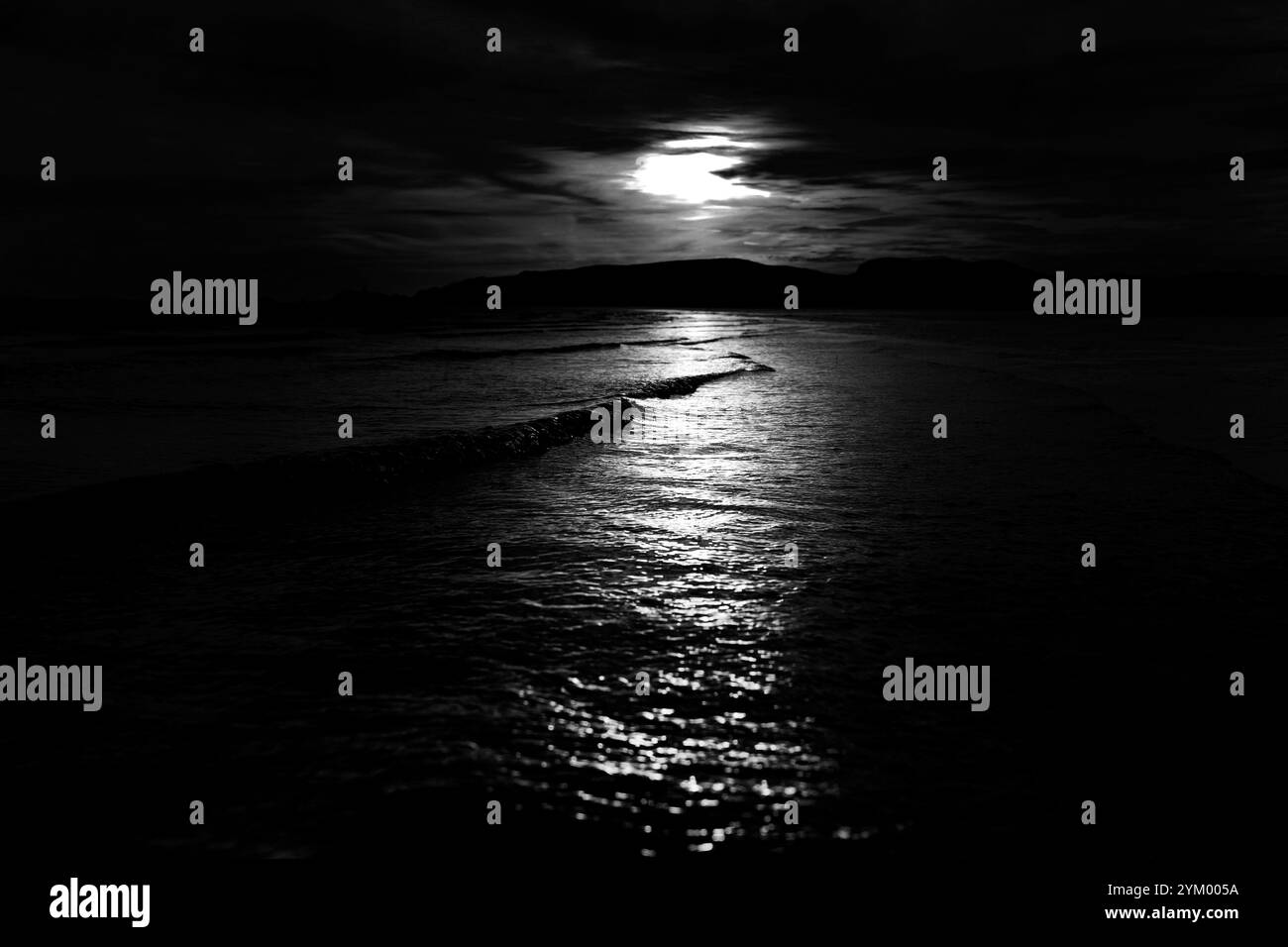 Fin de soirée, la lumière du soleil brille à travers les nuages sur la mer sur le rivage d'une plage. Photographie en noir et blanc. Banque D'Images