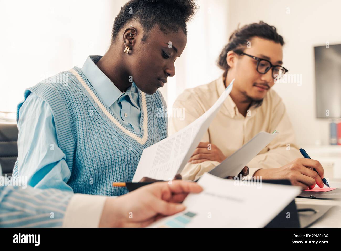 Équipe diversifiée de jeunes entreprises examinant des documents pendant la session de travail collaboratif dans le bureau moderne Banque D'Images