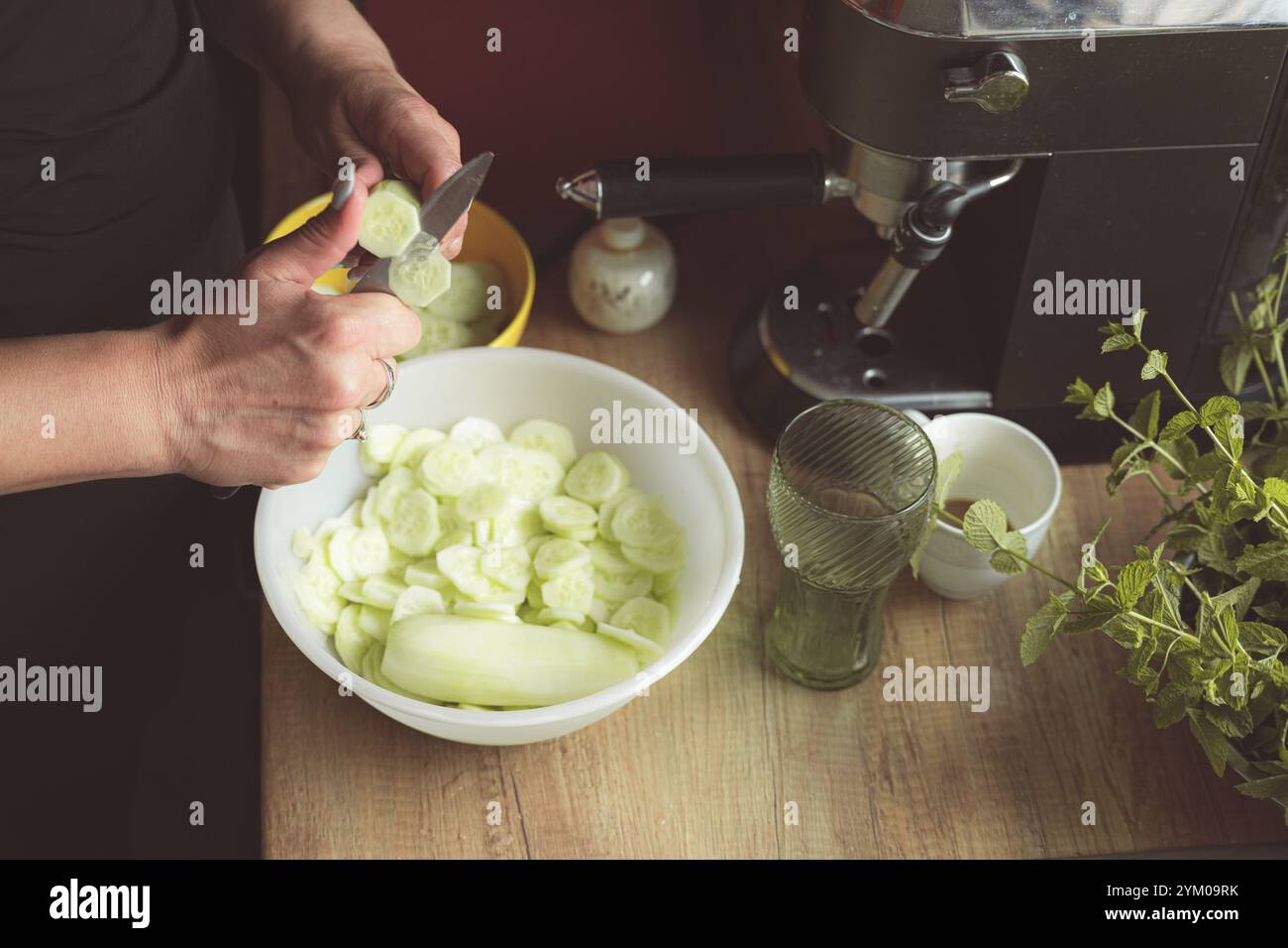 Cuisiner à la maison. Gros plan de la main femelle coupant le concombre dans un bol. Faire de la salade à partir de concombres frais du jardin de la maison. Alimentation saine. Préparation du repas Banque D'Images