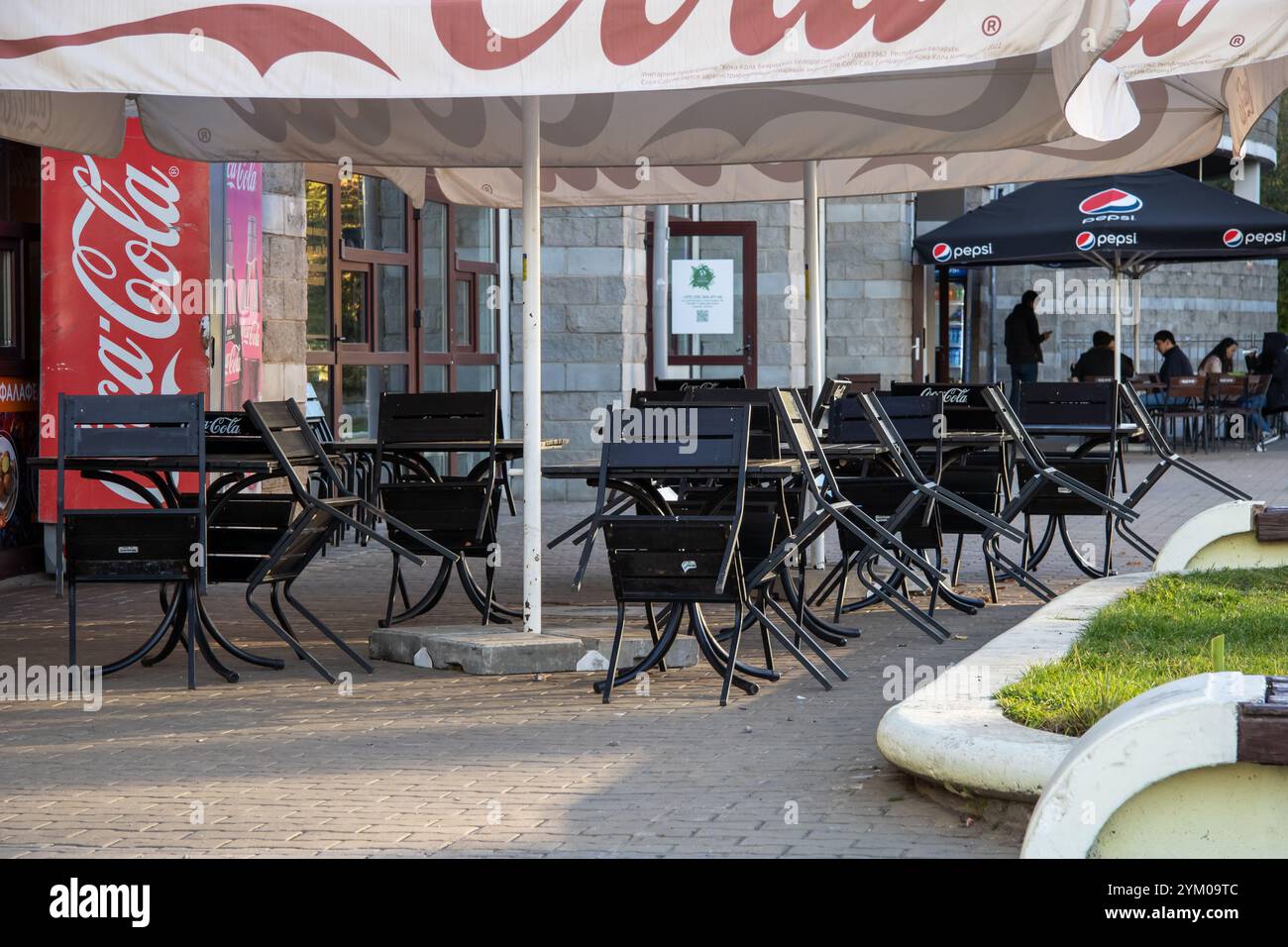 Biélorussie, Minsk - 29 octobre 2023 : sous un grand parapluie, il y a des tables et des chaises disposées, tandis qu'un distributeur automatique de coca cola se dresse prominentl Banque D'Images