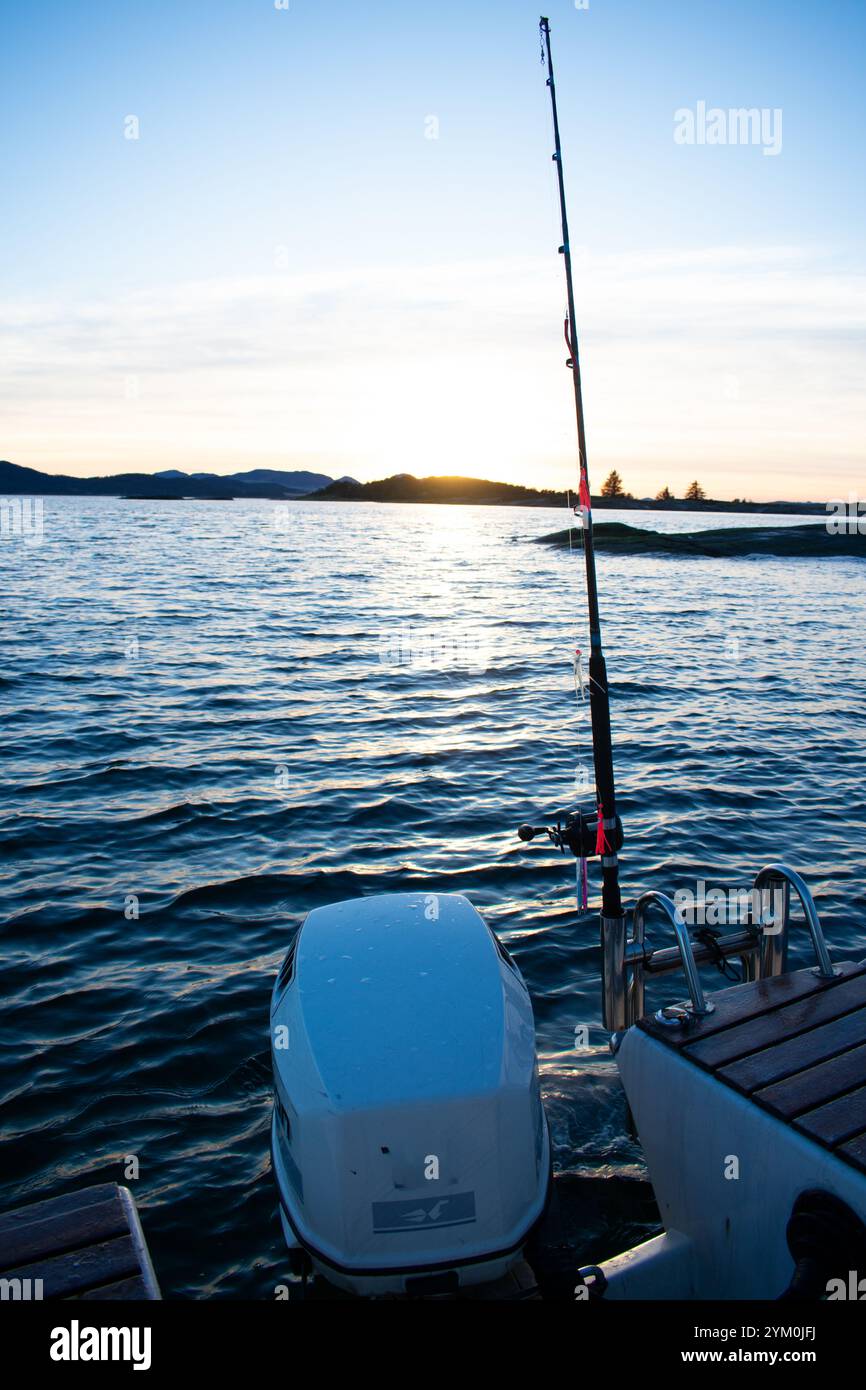 Bateau de pêche sur l'eau d'un fjord en Norvège pendant le coucher du soleil avec canne à pêche à l'arrière - Norway Vacations Banque D'Images