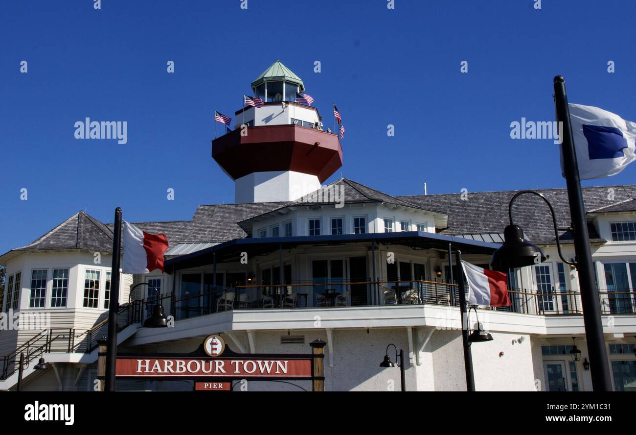 Hilton Head, Caroline du Sud, États-Unis - 21 février 2024 : une journée ensoleillée met en valeur le phare de Harbour Town et les bâtiments environnants avec des drapeaux fl Banque D'Images